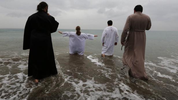 Menschen in Gewändern stehen im Wasser, möglicherweise bei einer religiösen Zeremonie.