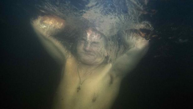 Ein Mann taucht unter Wasser, das Gesicht verzerrt.