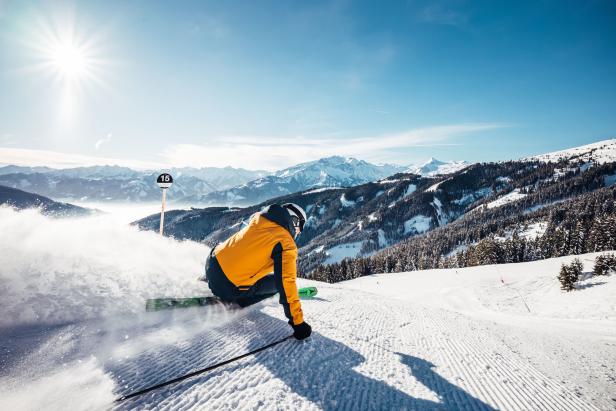 Ein Skifahrer fährt auf einer Skipiste mit Blick auf verschneite Berge.