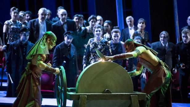 Zwei Darsteller schärfen ein Messer an einem Schleifstein auf einer Theaterbühne.