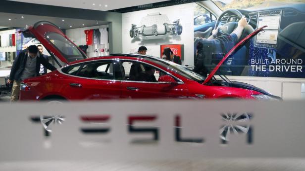 Ein rotes Tesla-Auto steht in einem Ausstellungsraum mit geöffneter Motorhaube und Kofferraum.