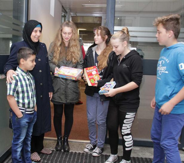 Eine Frau mit Kopftuch und eine Gruppe Kinder halten Spiele und ein Buch in den Händen.