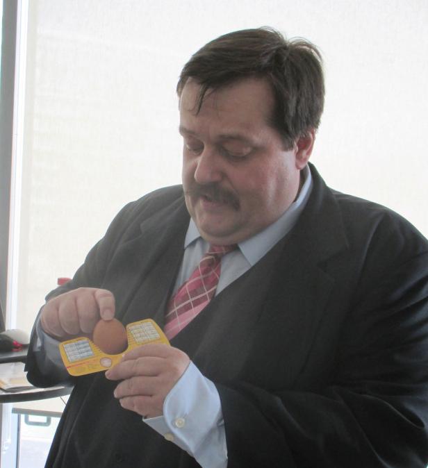 Ein Mann im Anzug hantiert mit einem Ei und einer gelben Eieruhr.