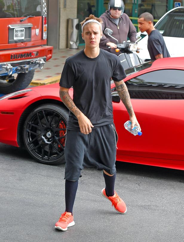 Justin Bieber steht vor einem roten Sportwagen und hält eine Wasserflasche.