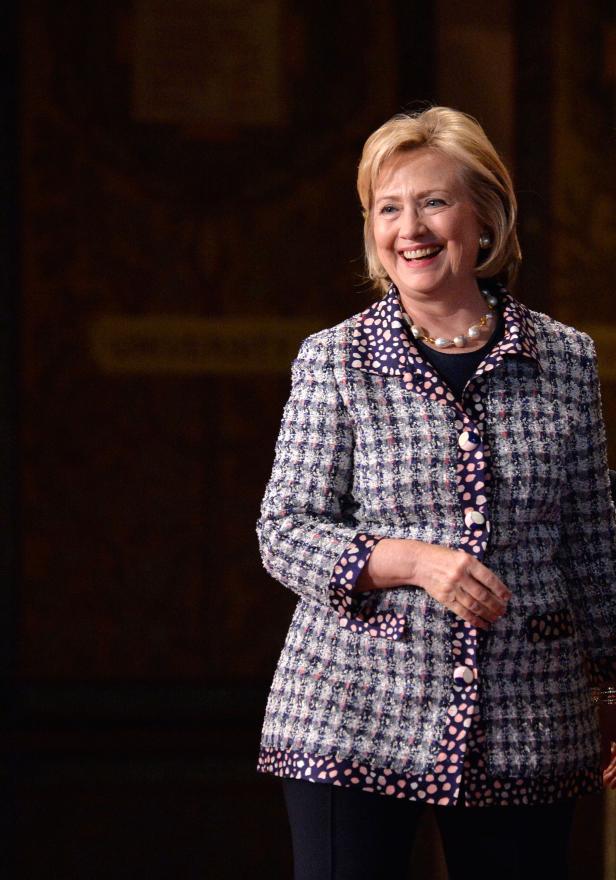 Hillary Clinton lächelt in einem gemusterten Blazer und einer Perlenkette.