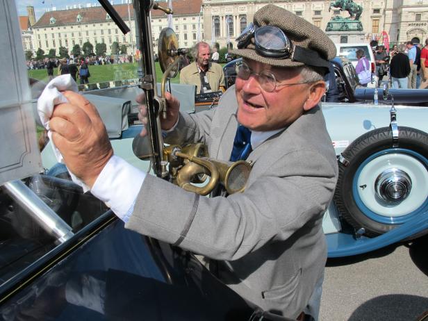 Ein Mann mit Mütze und Brille putzt ein Oldtimer-Auto mit einer Hupe.