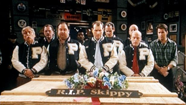 Eine Gruppe von Männern in Collegejacken steht an der Beerdigung von „Skippy“.
