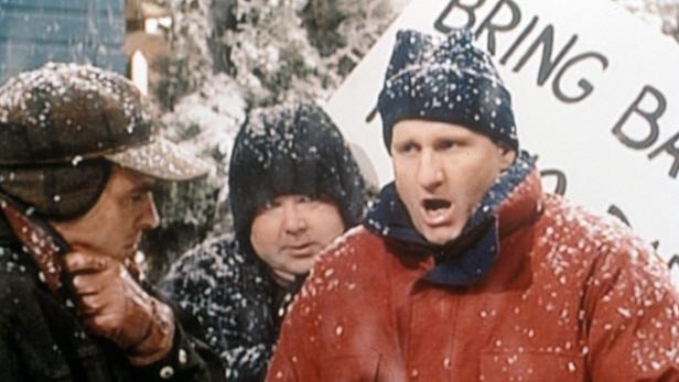 Drei Männer stehen im Schnee, einer von ihnen hält ein Schild mit der Aufschrift „Bring Back“.