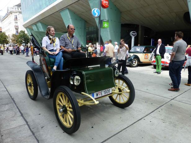 Ein Mann und eine Frau fahren in Wien in einem Oldtimer von 1906.