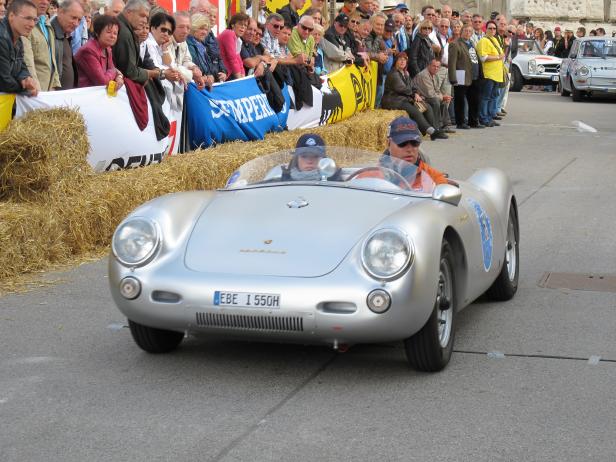 Ein silberner Porsche 550 Spyder fährt an einer Zuschauermenge vorbei.