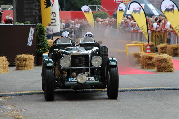 Ein grüner Oldtimer mit zwei Fahrern fährt auf einer abgesperrten Strecke.