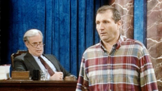 Al Bundy in einem karierten Hemd steht vor einem Mann im Anzug.