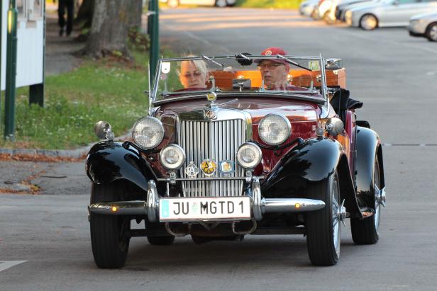 Ein Paar fährt in einem roten Oldtimer der Marke MG.