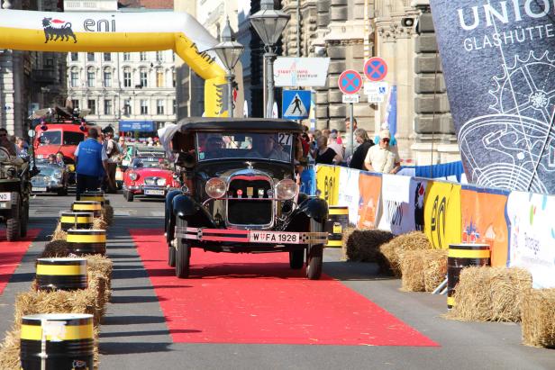 Ein Oldtimer fährt auf einem roten Teppich durch eine Stadt.
