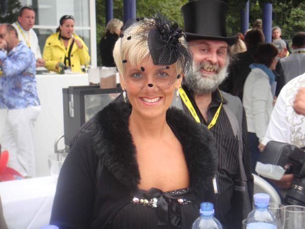 Eine lächelnde Frau mit Hut und Schleier, neben einem Mann mit Zylinder.