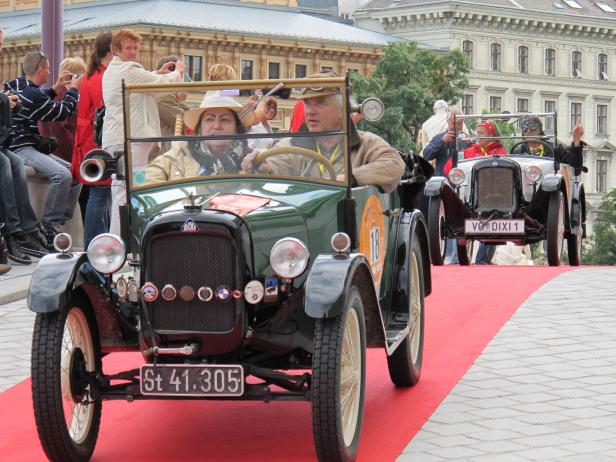 Ein grüner Oldtimer der Marke Dixi fährt über einen roten Teppich.