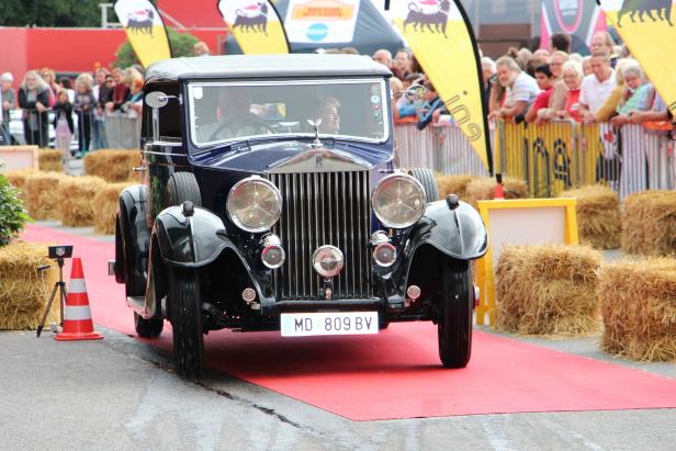 Ein blauer Oldtimer von Rolls-Royce fährt über einen roten Teppich.