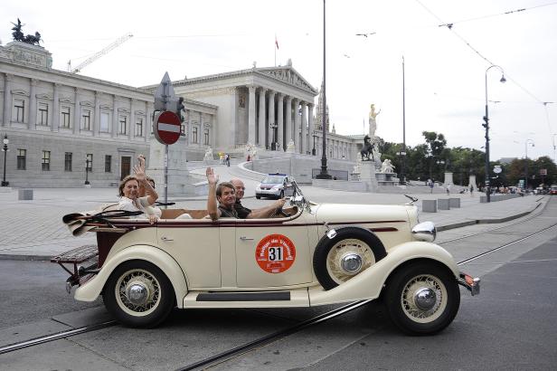 Ein Oldtimer-Cabriolet mit zwei Personen vor dem österreichischen Parlament in Wien.