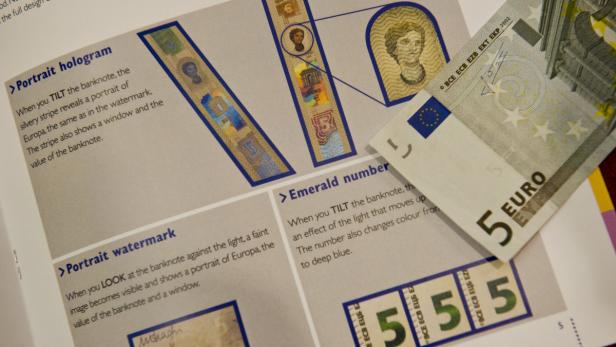 Eine 5-Euro-Banknote liegt auf einer Broschüre, die Sicherheitsmerkmale von Euro-Banknoten erklärt.