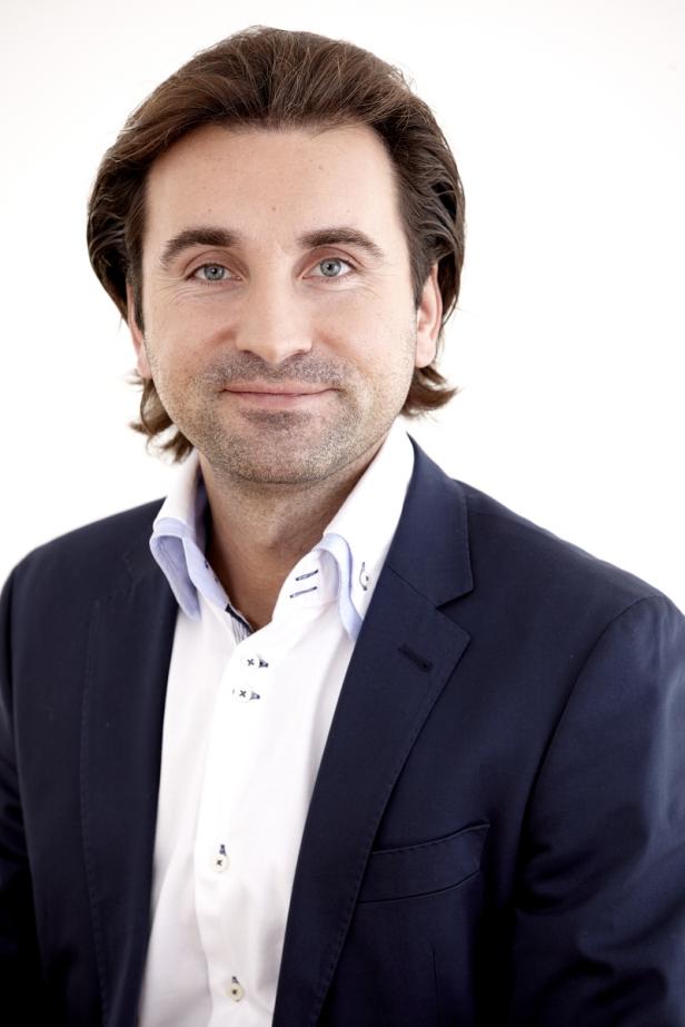 Ein Mann mit braunen Haaren und blauem Hemd blickt in die Kamera.