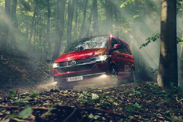 Ein roter VW-Bus fährt durch einen nebligen Wald.
