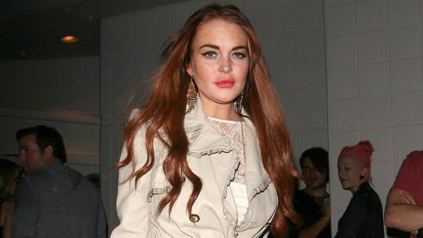 Lindsay Lohan trägt einen Trenchcoat und lange Ohrringe.