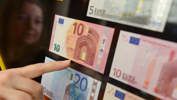 Eine Hand zeigt auf einen 10-Euro-Schein, umgeben von anderen Euro-Banknoten.
