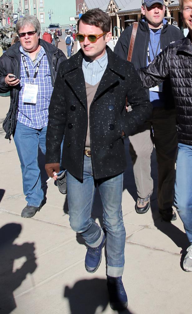 Elijah Wood mit Sonnenbrille und dunkler Jacke geht die Straße entlang.