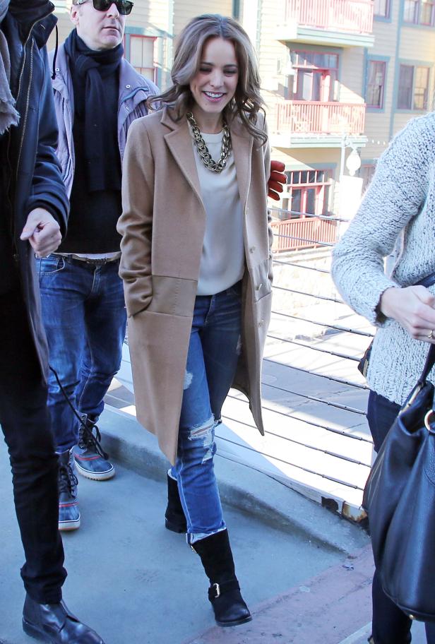 Rachel McAdams in einem beigen Mantel und zerrissenen Jeans lächelt.