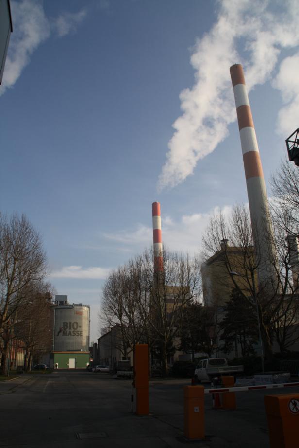 Ein Biomasseheizkraftwerk mit rot-weiß gestreiften Schornsteinen unter blauem Himmel.