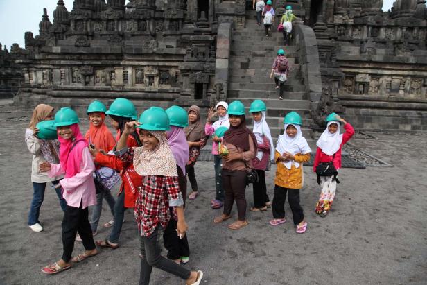 Eine Gruppe junger Frauen mit Kopftüchern und Bauhelmen vor einem Tempelgebäude.