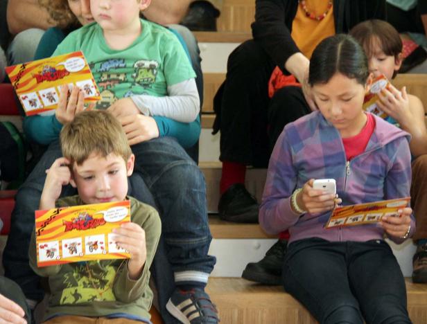 Eine Gruppe Kinder sitzt auf einer Treppe, einige lesen, ein Mädchen benutzt ein Smartphone.