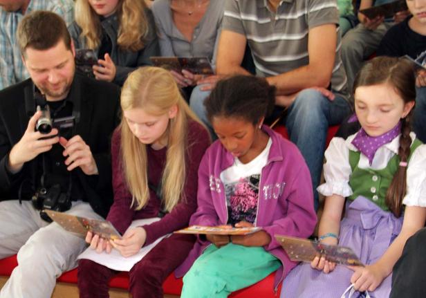 Eine Gruppe von Kindern und Erwachsenen sitzt und betrachtet Broschüren.