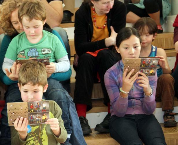 Eine Gruppe Kinder sitzt auf einer Treppe und betrachtet kleine Bilderbücher.
