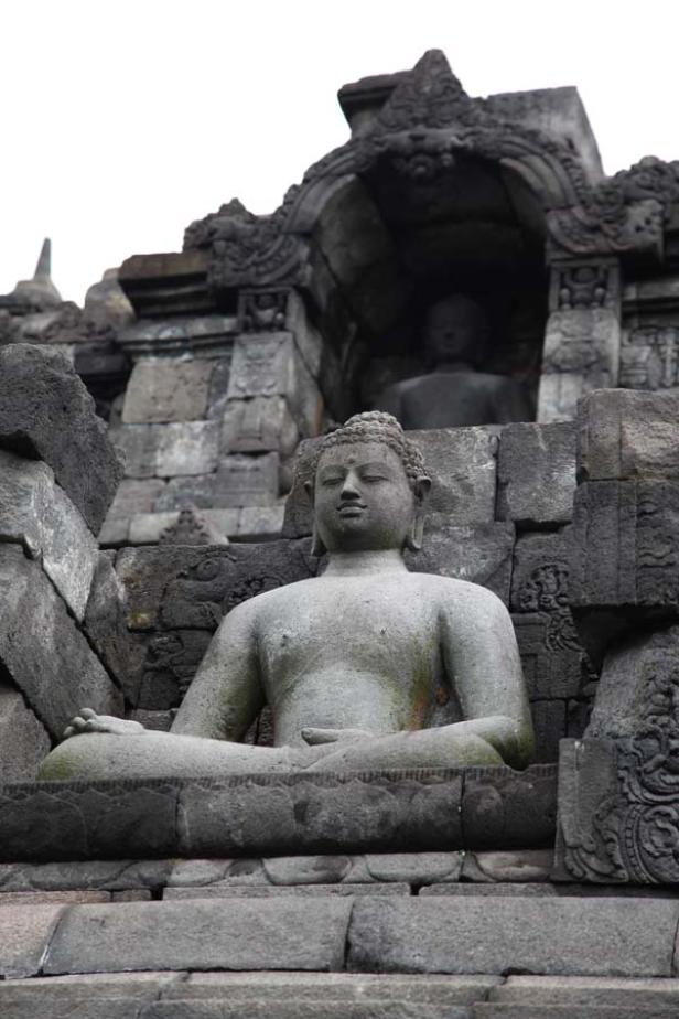 Eine Buddha-Statue sitzt inmitten der Ruinen eines alten Tempels.