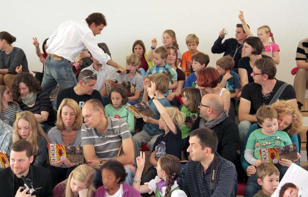 Ein Mann verteilt Bücher an eine Gruppe von Kindern und Erwachsenen.