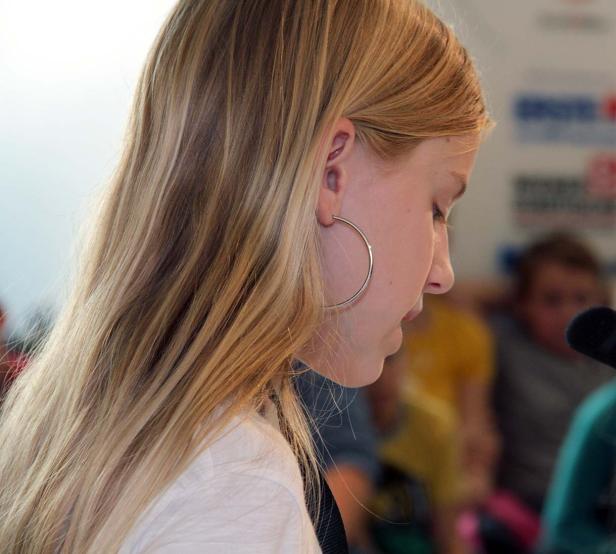 Eine junge Frau mit blonden Haaren und einem Ohrring blickt nach unten.
