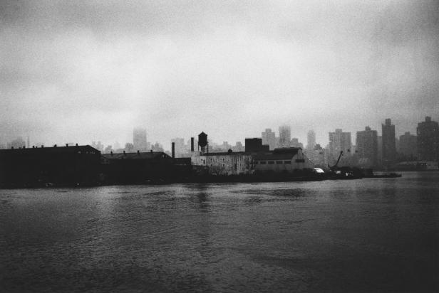 Eine Schwarzweißaufnahme einer Stadtlandschaft am Wasser unter einem trüben Himmel.