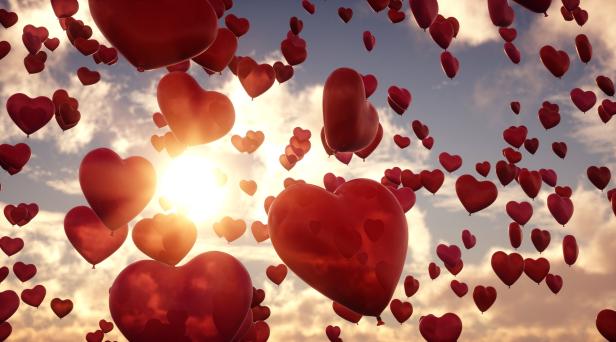 Viele rote Herzballons steigen vor einem bewölkten Himmel auf.