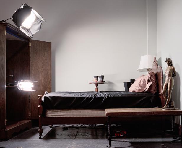 Ein Schlafzimmer mit einem Bett, einem Schrank, einer Statue und Beleuchtung für ein Fotoshooting.