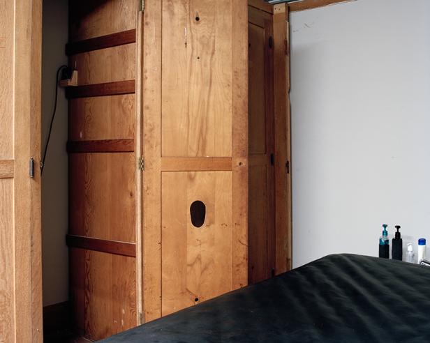 Ein hölzerner Eckschrank steht in einem Raum neben einer Liege.