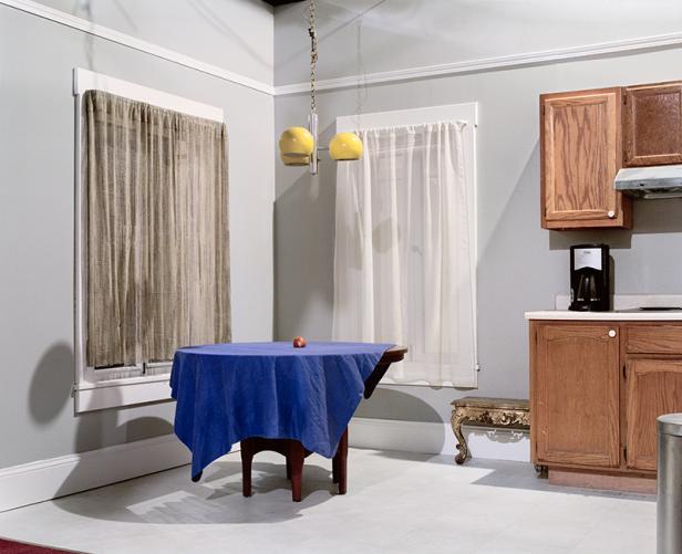 Ein gedeckter Tisch mit blauem Tuch und Apfel in einem Raum mit Küchenzeile.