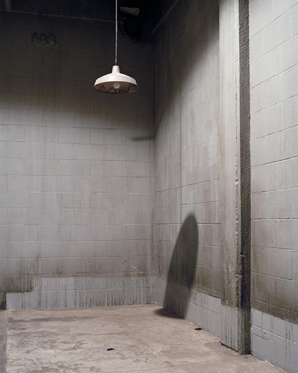 Eine nackte Glühbirne hängt in einem leeren, feuchten Kellerraum.