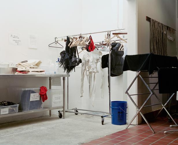 Ein Raum mit Kleidung an einer Stange, einem Trockengestell und Behältern mit der Aufschrift „Dirty Latex and Leather“.