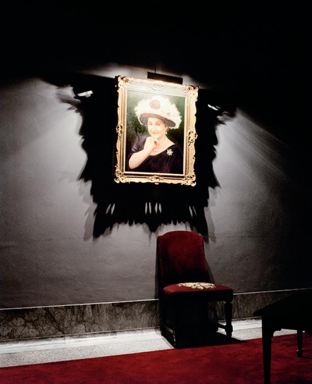 Ein Porträt einer Frau mit Hut hängt über einem roten Stuhl.