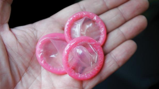 Eine Hand hält drei verpackte, pinkfarbene Kondome.