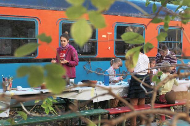 Kinder und Erwachsene basteln an Tischen vor einem orange-blauen Zugwaggon.