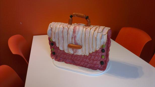 Eine ungewöhnliche Handtasche aus Wurst, Speck und Oliven auf einem Tisch.