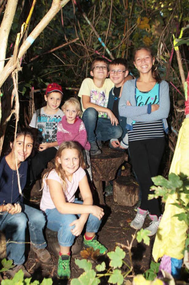 Eine Gruppe von sieben Kindern posiert in einem selbstgebauten Unterschlupf im Wald.