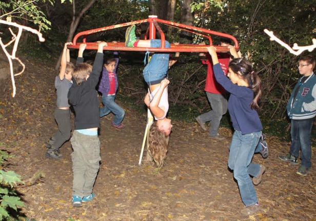 Eine Gruppe Kinder spielt auf einem Spielplatzkarussell, ein Mädchen hängt kopfüber.